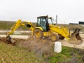 A yellow backhoe loader repairing and cleaning the edges of a road performing conservation work Royalty Free Stock Photo