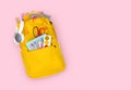 Yellow backpack with school supplies isolated on pink background