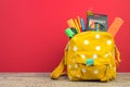 Yellow backpack with white polka dots with different colorful stationery on table. Bright Red background. Back to school Royalty Free Stock Photo