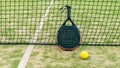 Yellow ball on grass turf near padel tennis racket behind net in green court Royalty Free Stock Photo