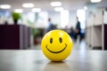 Yellow ball with happy smiling face with blurry office in background. Concept for happines at work