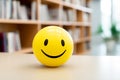 Yellow ball with happy smiling face with blurry office in background. Concept for happines at work