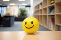 Yellow ball with happy smiling face with blurry office in background. Concept for happines at work