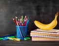 yellow banana on a stack of notebooks, a blue stationery glass with multi-colored wooden pencils Royalty Free Stock Photo