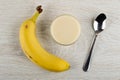 Banana, glass bowl with condensed milk, spoon on wooden table. Top view