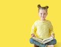 Funny child girl yellow jacket on a yellow background, sitting, reading a book, development and school concept Royalty Free Stock Photo