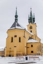 Yellow baroque church of St. James the Elder with gothic clock tower, medieval historical buildings, Main town square under snow