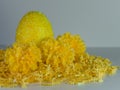 Yellow Beaded Easter Egg sitting on a bed of yellow paper shreds with 3 yellow carnation flower blooms on a white background