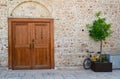 Yellow bicycle and tub with a tree against a stone wall with a large wooden door Royalty Free Stock Photo