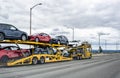 Yellow big rig car hauler semi truck transporting cars on two level hydraulic semi trailer driving on the wide highway road