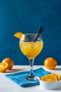 Yellow bird cocktail with rum, orange and lime juice, oranges, blue napkin. White table. Dark blue background. Royalty Free Stock Photo