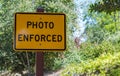 A yellow and black metal sign saying `Photo Enforced` in the woods with copy space