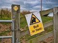 A yellow and black sign fixed to a wooden fence warns walkers of a bull loose in a field ahead Royalty Free Stock Photo