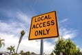 Yellow and black square road sign in neighborhood reading Local Access Only against a blue sky with palm trees