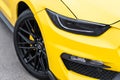 Yellow with black stripes Ford Mustang muscle car in a parking lot. Close-up of headlight and wheel