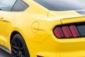 Yellow with black stripes Ford Mustang muscle car in a parking lot. Close-up of headlight and wheel