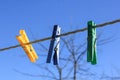 A Yellow and a blue and green clothes peg are clipped at different angles, set against the backdrop of a bright blue sky Royalty Free Stock Photo