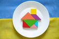 The yellow-blue national flag of Ukraine as a background and a children's house made of cubes lies in a plate, stop