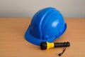 A yellow and blue plastic flashlight with a blue hard hat isolated against a wooden background Royalty Free Stock Photo