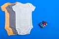 Yellow bodysuit, gray bodysuit and green bodysuit made of cotton with a child`s toy. Clothes for newborns on a blue background Royalty Free Stock Photo