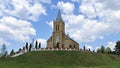 The yellow brick church with a tower and metal roof stands on a grassy hill and is surrounded by a metal and stone fence. A stairc Royalty Free Stock Photo