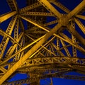 The yellow bridge lanterns illuminated by a steel bridge farm against a dark blue evening sky.