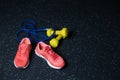 Crimson bright sneakers, yellow vivid dumbbells, blue expander, equipment for a workout on a dark blurred background. Royalty Free Stock Photo