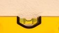 Yellow bubble level showing bubble in the level position to indicate a flat plane, resting against a white painted wall Royalty Free Stock Photo