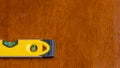 Yellow bubble level showing bubble in the level position to indicate a flat plane, resting on a brown wooden surface Royalty Free Stock Photo