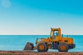 Yellow bulldozer on the background of clear blue sky and sea. Copy space