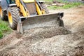 A yellow bulldozer or a loader actively digging dirt in a field under a blue sky on a clear day