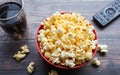 Popcorn butter flavor in red bowl with a glass of cola and TV remote control on wooden background Royalty Free Stock Photo