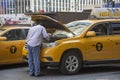 Yellow cab driver looking at engine of his taxi Royalty Free Stock Photo