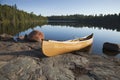 Yellow canoe on rocky shore of calm lake with pine trees