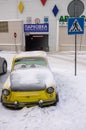 A yellow car, covered with snow, standing near a shopping center. Royalty Free Stock Photo