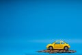 Yellow car figurine placed on top of a heap of golden coins, on blue background