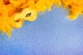 Yellow carnival mask and feather boa on blue background with copy space. Blank for a holiday card Royalty Free Stock Photo