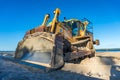 Yellow Caterpillar earth mover, digger with shiny metal shovel on sandy beach