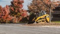 Yellow caterpillar loader collecting the fallen dry leaves from the street in autumn