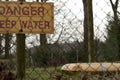 Yellow caution sign with the meesage of Danger, Deep Water behind the metal fence in the forest Royalty Free Stock Photo