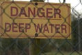 Yellow caution sign with the message Danger, Deep Water written in red behind the metal fence