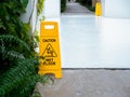 Yellow caution slippery wet floor sign with slippery person warning icon on wet white concrete floor background. Royalty Free Stock Photo