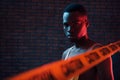 Yellow caution tape and uniform. Futuristic neon lighting. Young african american man in the studio Royalty Free Stock Photo