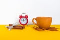 Yellow ceramic coffee cup and cinnamon stick on the background of an alarm clock with an autumn maple leaf. The concept of the Royalty Free Stock Photo