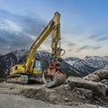 yellow chain excavator with grapple of natural stone in front of a mountain backdrop