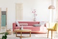 Yellow chair next to pink sofa and wooden table in pastel living