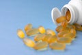 Yellow chewable capsules with fish oil in plastic white jar are lying on blue background.