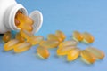 Yellow chewable capsules with fish oil in plastic white jar are lying on blue background