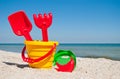 Yellow child pail with a red handle, plastic red spatula and rake, and a plastic green sieve, a red sand form in the form of a ban Royalty Free Stock Photo
