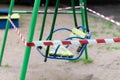 Yellow children\'s swing on a sports playground in the park wrapped with red barrier tape